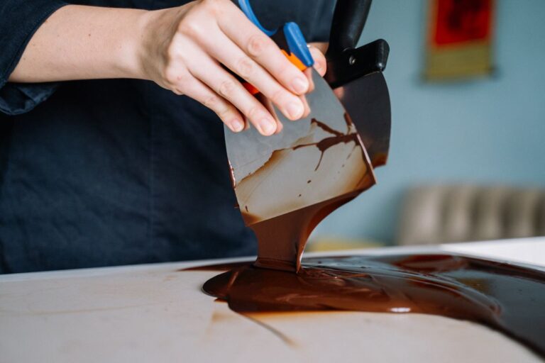 Chocolatier tempereert chocolade met een spatel op een werkblad